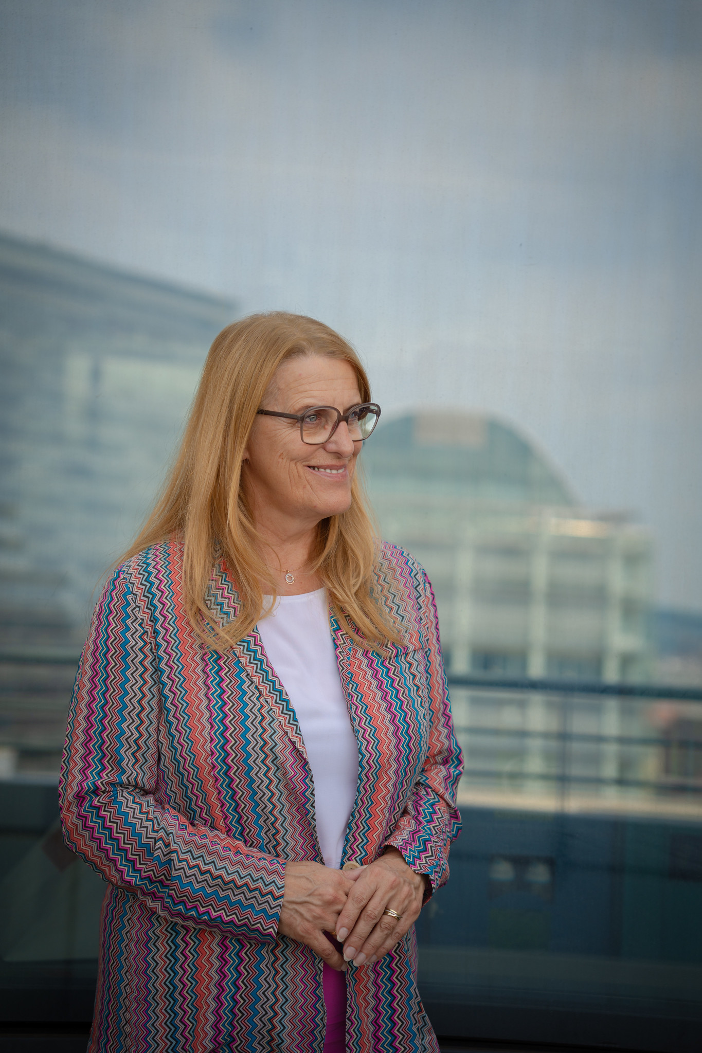 Ulrike Königsberger-Ludwig mit Brille und gemustertem Blazer vor einer Glasfassade.