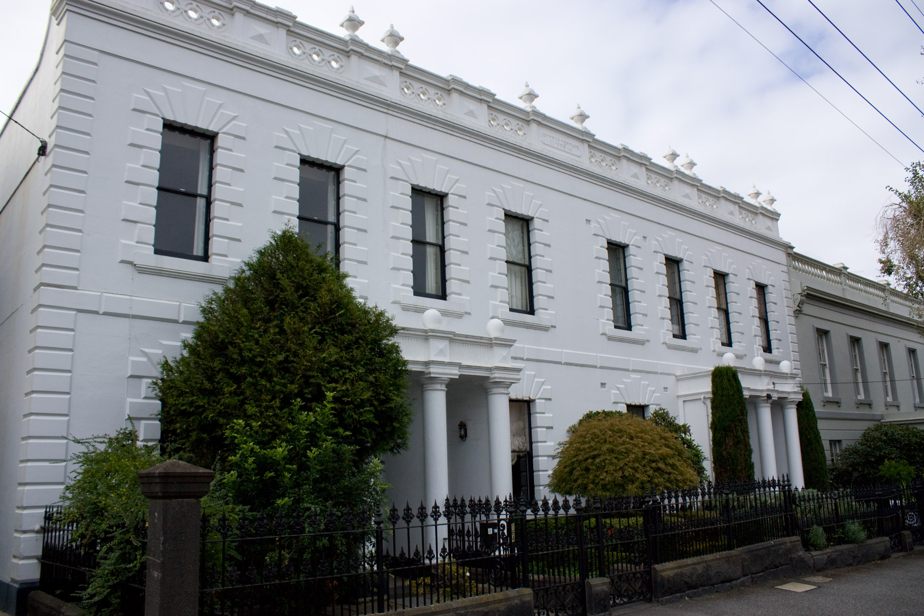 A row of white terraced houses with gardens and iron fences in Melbourne.